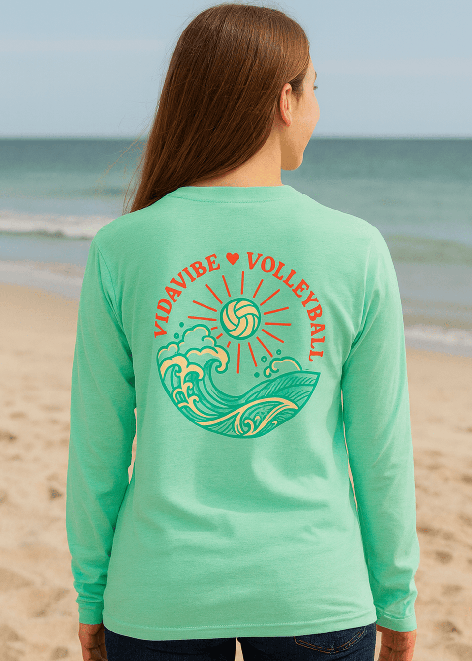 Person wearing a green long-sleeve shirt with a volleyball design on a beach